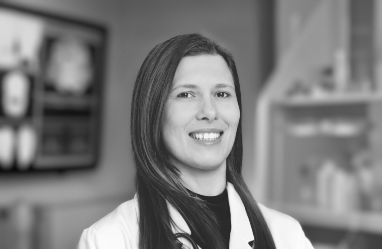 Dr. Nev Zubcevik smiling at the camera while wearing a lab coat in a doctor's office